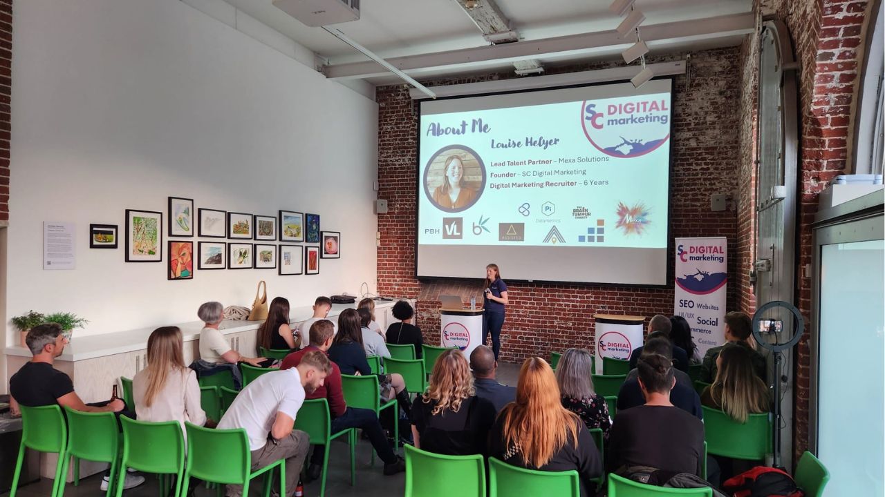 host louise stood at the front of the room with an audience talking